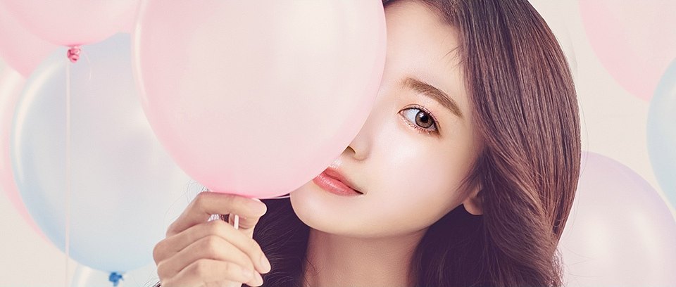 파스텔 톤 분홍 풍선 뒤에서 한쪽 눈만 드러낸 채 정면을 바라보는 여성의 얼굴 클로즈업