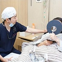 수술캡을 쓴 의료진이 침대에 누운 환자에게 사후 관리 장비를 적용하는 모습