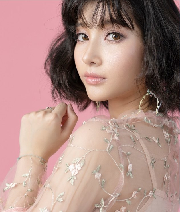 레이스 드레스를 입은 여성이 어깨를 감싸며 카메라를 바라보는 상반신 사진