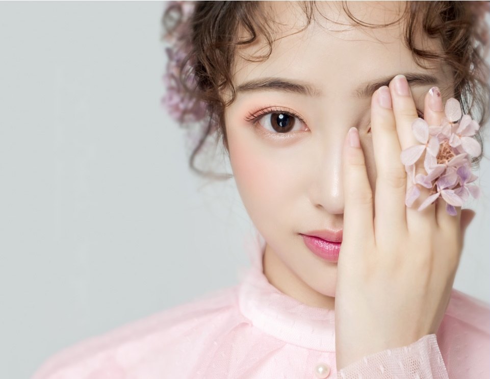 분홍 니트를 입은 여성 모델이 한 손으로 한쪽 눈을 가리고 또렷한 쌍꺼풀 눈매를 보여주는 클로즈업.