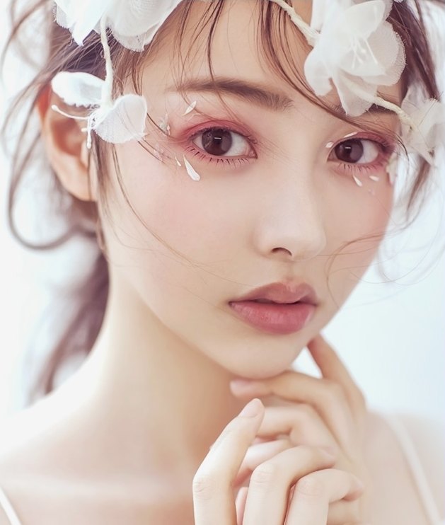 흰 꽃 장식을 머리에 얹고 턱에 손끝을 댄 채 정면을 바라보는 여성 모델