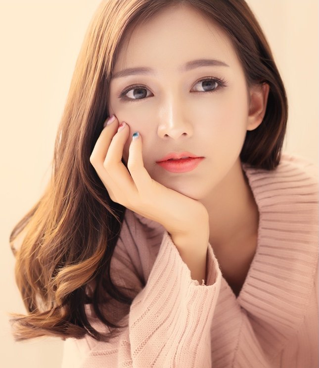 분홍 니트를 입은 여성이 턱을 괴고 정면을 바라보는 모습