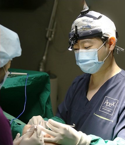헤드라이트 루페와 마스크를 착용한 집도의가 초록 수술포가 깔린 수술대에서 눈 수술을 집도하는 장면