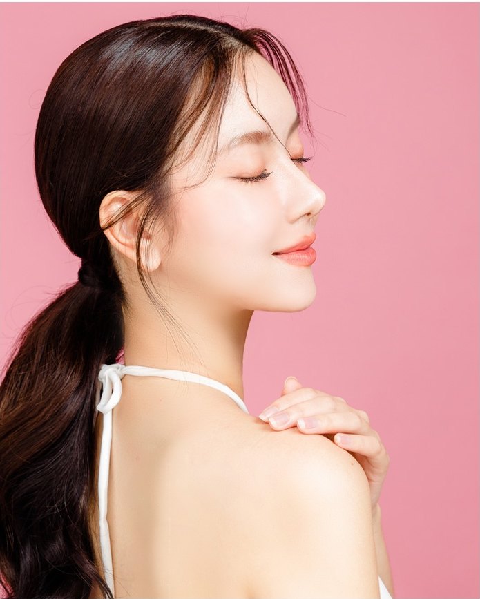 분홍 배경 앞에서 눈을 감고 옅게 미소 짓는 여성 모델의 옆얼굴.