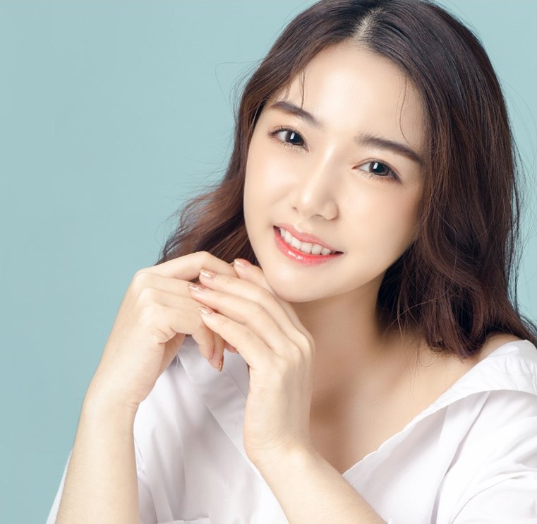 두 손을 턱 아래로 모으고 환하게 웃는 여성 모델
