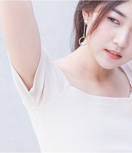 흰 니트 탑을 입은 여성이 한쪽 팔을 들어올린 채 고개를 돌리고 있는 모습