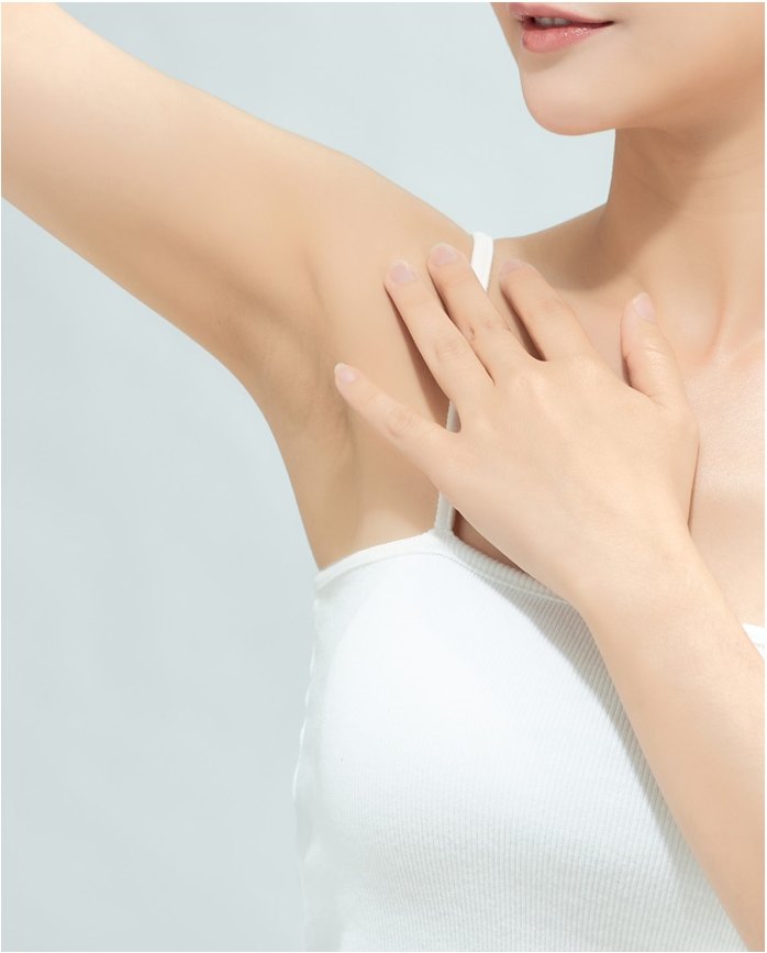 흰 슬리브리스를 입은 여성이 한 팔을 들어 반대편 손으로 쇄골과 겨드랑이 부위를 짚고 있는 모습