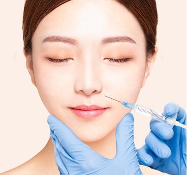 파란색 라텍스 장갑을 낀 시술자가 눈을 감은 여성의 팔자 부위에 가는 주사기로 지방을 주입하고 있다